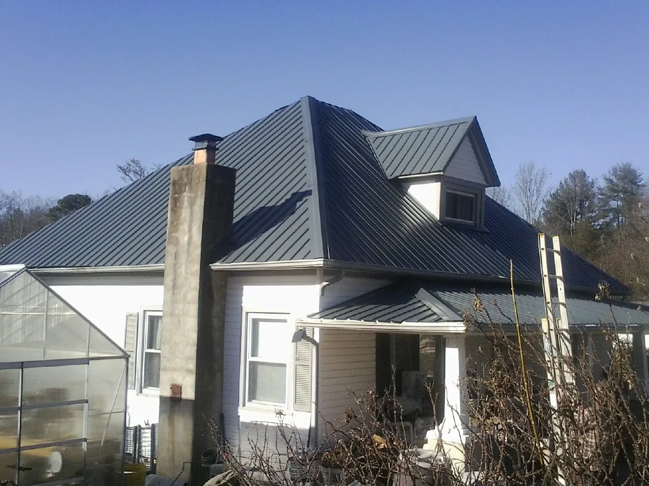 Dark blue standing seam metal roof on a white farmhouse with dormer — Slate & Tile Roof Repair by Roofing Brothers in Barstow