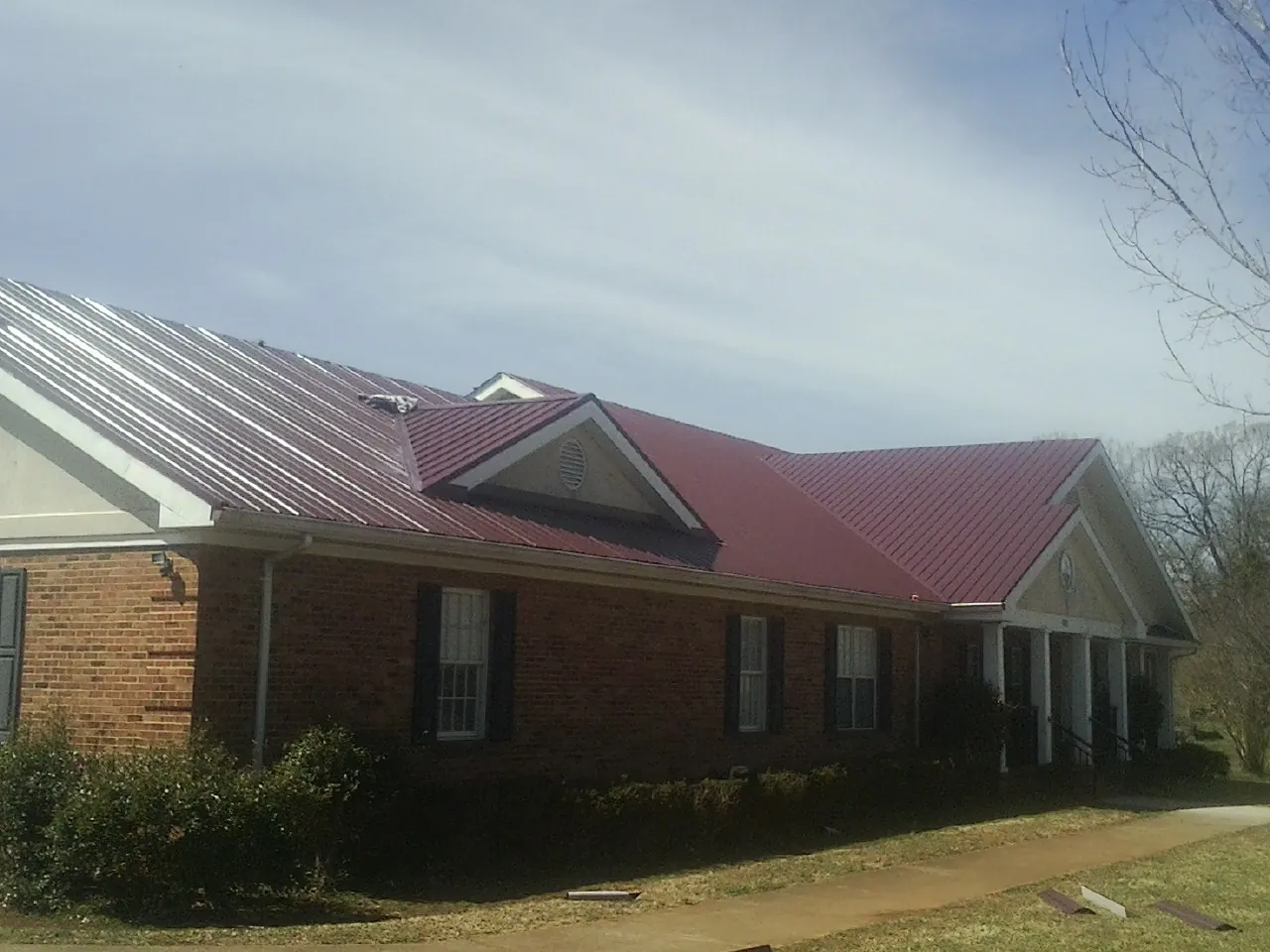 Red metal roof with gabled entries on a long brick building, from a Hail Damage Roof Repair job in Barstow