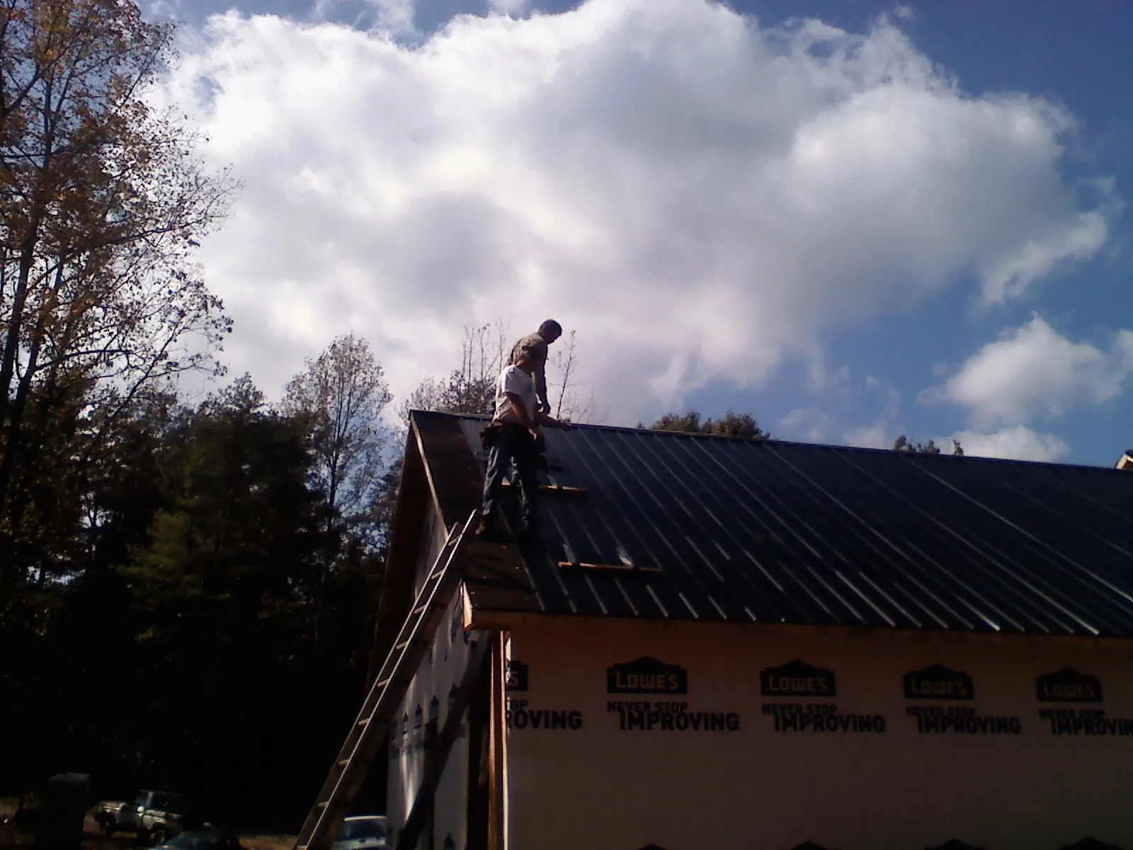 Roofer fastening dark metal panels high against a cloudy sky, from a Roof Inspection job in Barstow