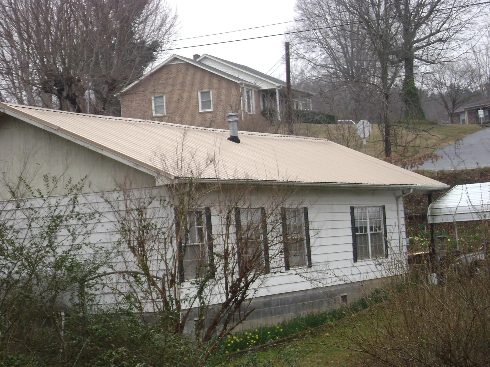 Tan metal roof on a white sided house set into a hillside — Commercial Roofing by Roofing Brothers in Barstow