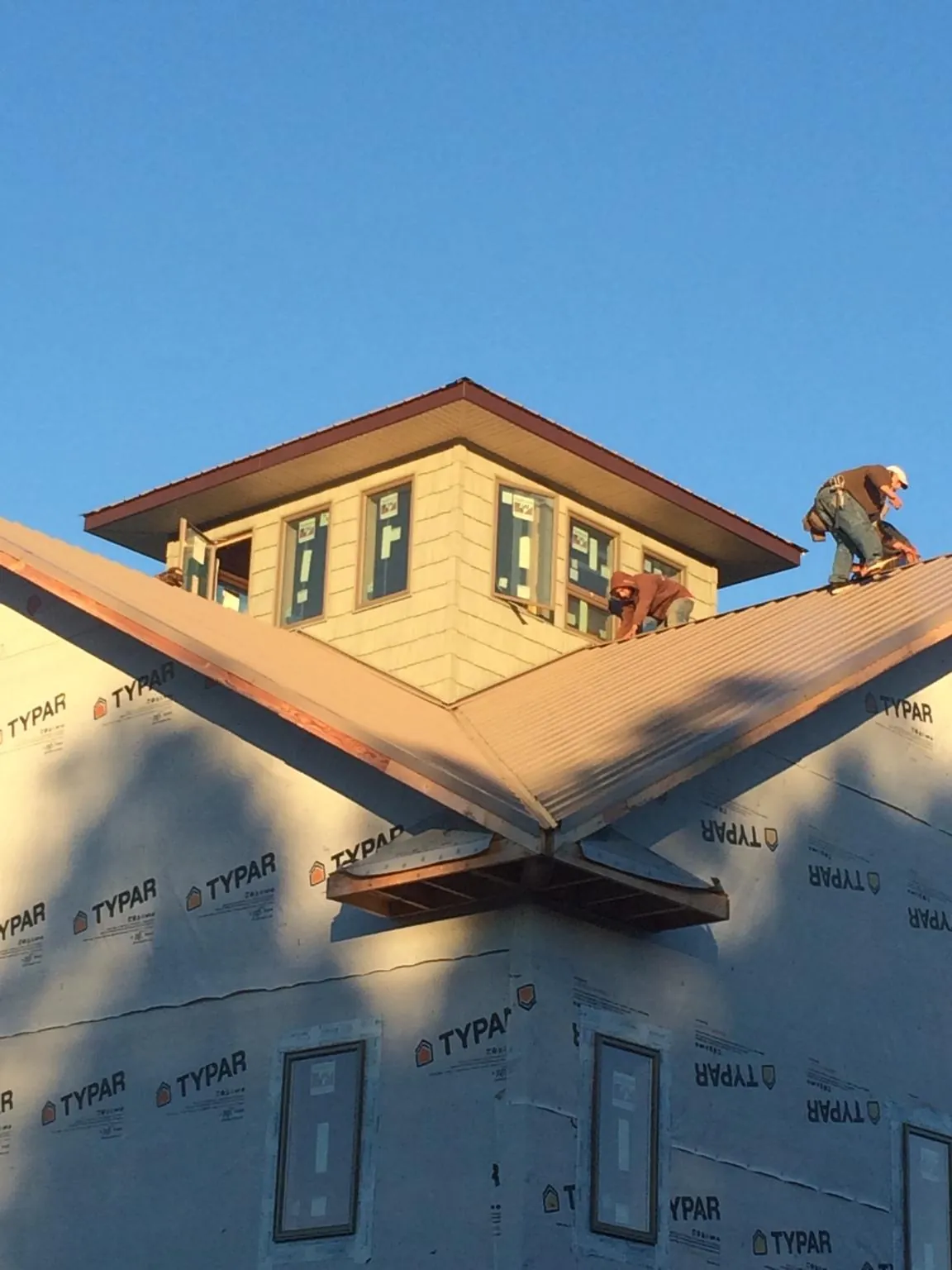 Roofers working around a rooftop cupola on a new metal roof at sunset — Roof Waterproofing in Barstow by Roofing Brothers